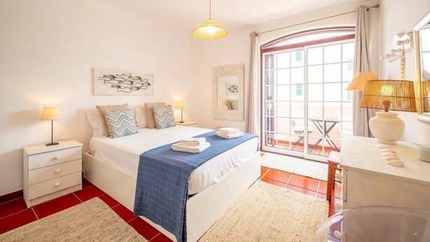 Un dormitorio con cama, mesitas de noche, lámpara, espejo y ventana con vistas.