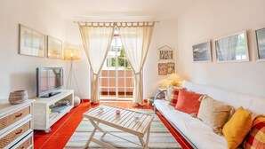 Una sala de estar con sofá, televisión y ventana con cortinas.