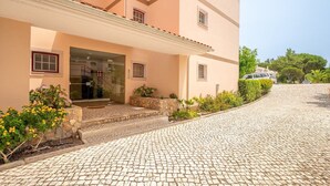 Un edificio de varios pisos con fachada de piedra y un camino pavimentado, con un vehículo estacionado al fondo.