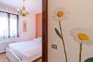 A bedroom with a bed, a chandelier, a window with curtains, and a wall with a daisy painting.