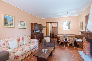 Ein Wohnzimmer mit einer Couch, Sesseln, einem Couchtisch, einem Essbereich mit Tisch und Stühlen sowie einem Kamin.