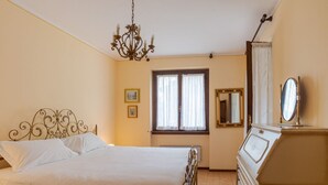 Ein Schlafzimmer mit einem Bett, einem Schminktisch, einem Spiegel, einem Fenster mit Vorhängen und einer Kristallleuchtre.