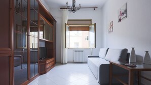 Une pièce comprenant un canapé, une table, un meuble avec des portes en verre, un radiateur et une fenêtre avec des rideaux.
