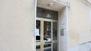 Une entrée d’immeuble avec une porte en verre, une caméra de surveillance au-dessus, et un panneau indiquant « ENVOYER » sur le mur.