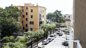 Un immeuble jaune à plusieurs étages, doté de balcons, entouré d’arbres et de voitures garées.