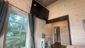 Une chambre avec une grande fenêtre, des murs en bois, un lit, une table de chevet et une porte donnant sur une douche.