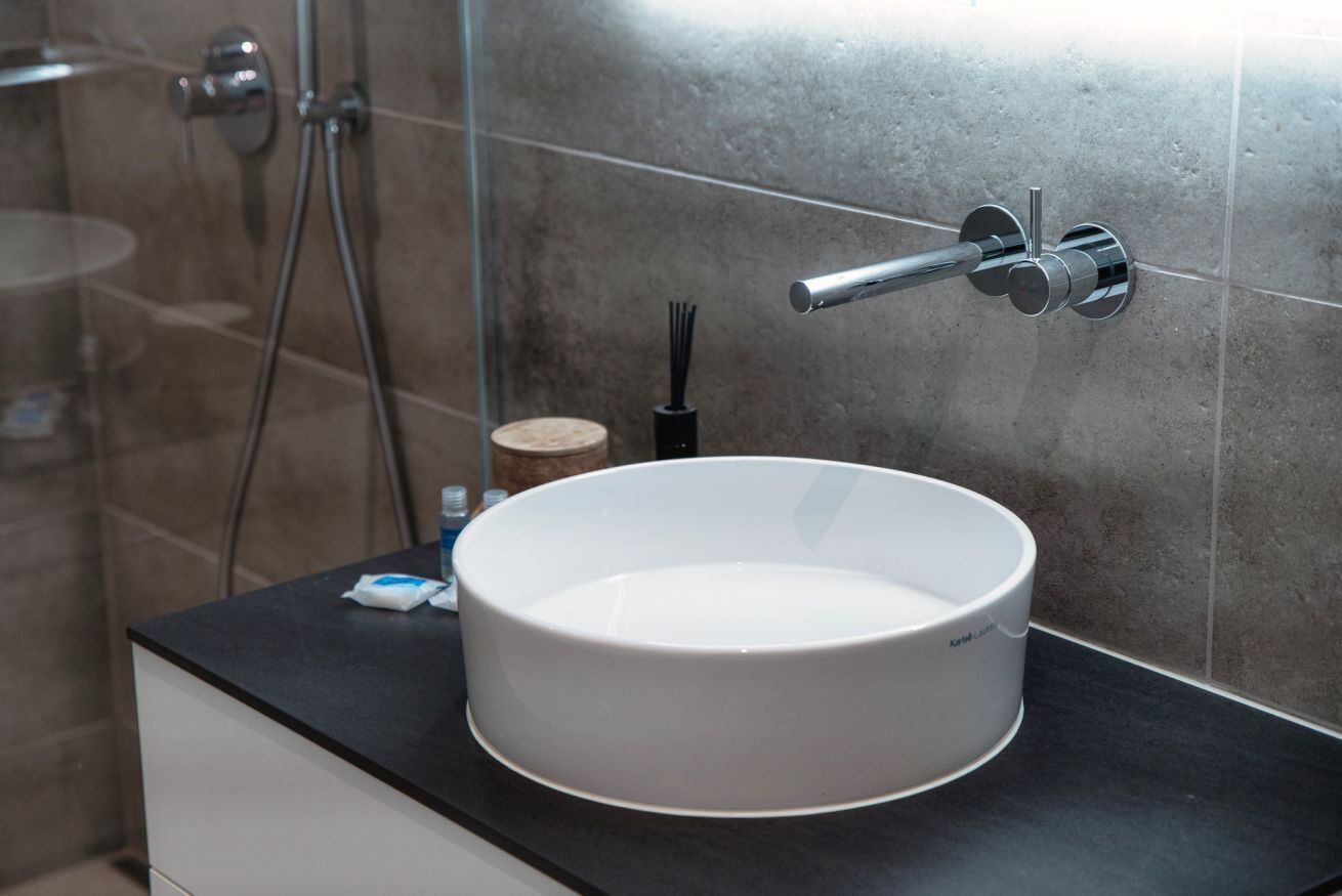 Un baño con un lavabo blanco redondo, un cabezal de ducha de mano y un perchero para toallas.