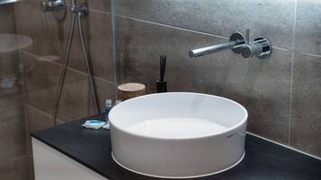Un baño con un lavabo blanco redondo, un cabezal de ducha de mano y un perchero para toallas.