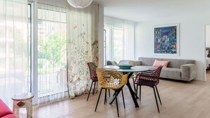 Un salon moderne avec un coin repas, comprenant un canapé, une table avec des chaises et une grande fenêtre agrémentée de rideaux légers.