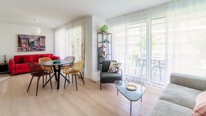 Un salon moderne avec un canapé rouge, un fauteuil gris, une table à manger avec des chaises et un balcon offrant une vue dégagée.