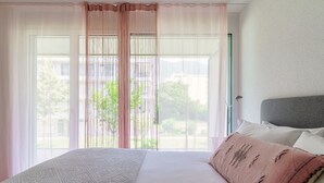 Une chambre à coucher avec un lit, une fenêtre ornée de rideaux légers et une vue sur la verdure environnante.