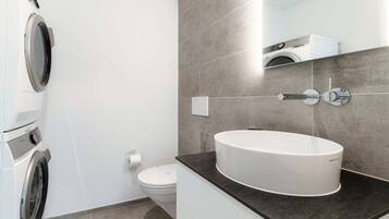 Un baño moderno con lavadora incorporada, un inodoro y un lavamanos grande con espejo.