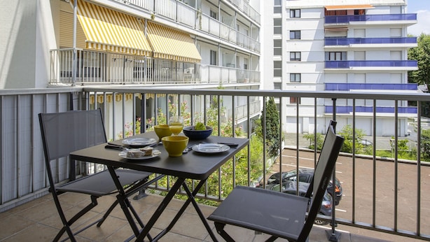 A balcony with a table set for two, a yellow and white striped awning, and a view of a multi-story building with balconies. - Appartement Herta - Welkeys (Biarritz)