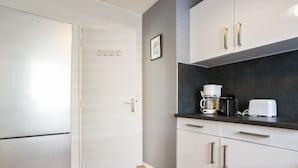 A compact kitchen with a refrigerator, a coffee maker, and a toaster on the countertop. - Appartement Herta - Welkeys (Biarritz)