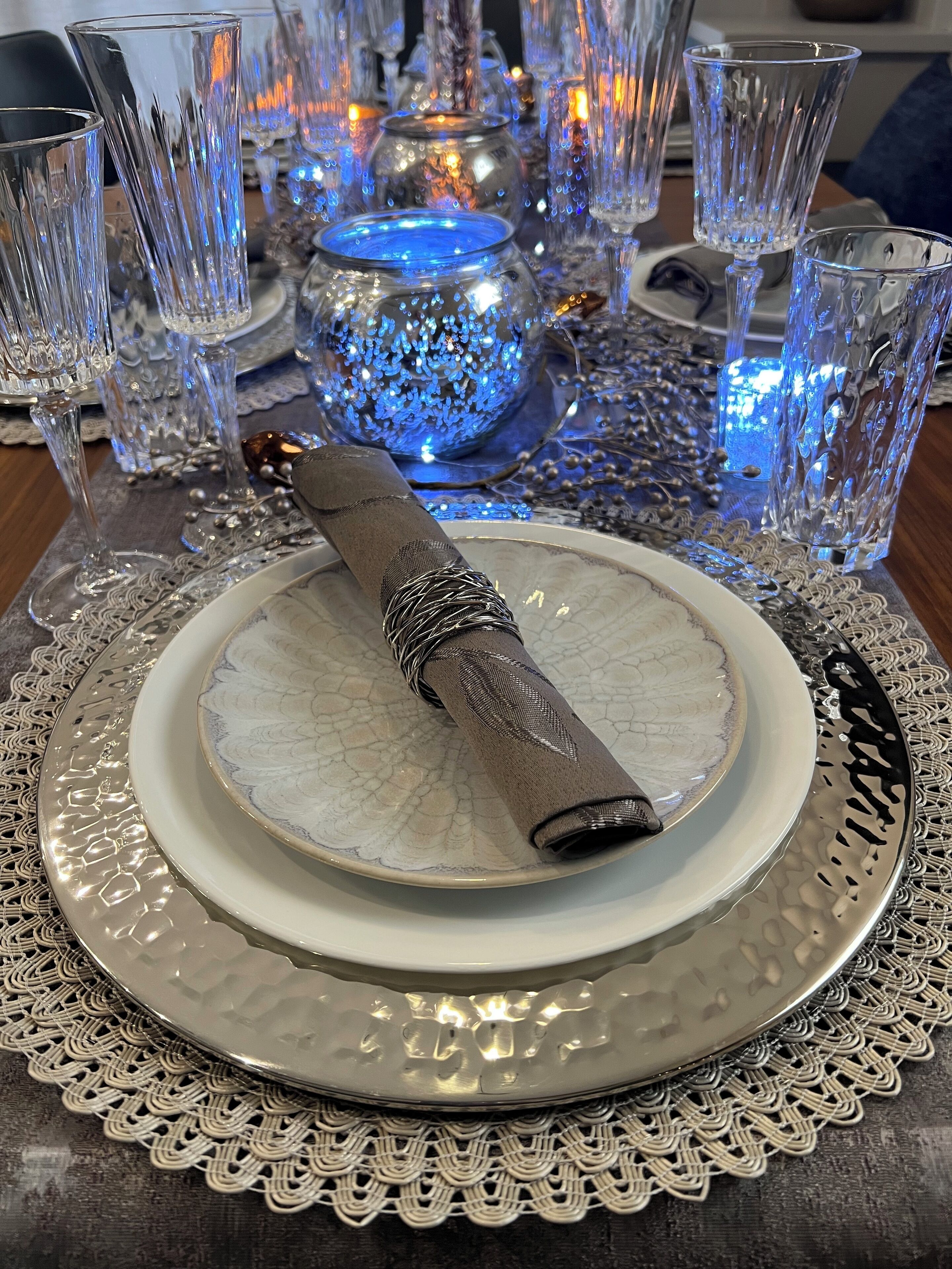 Una mesa dispuesta con un plato blanco, un plato bajo de plata y una servilleta doblada.