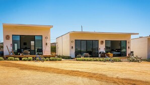Dos edificis moderns amb grans portes i finestres de vidre, un sòl de terra i bicicletes aparcades al davant.