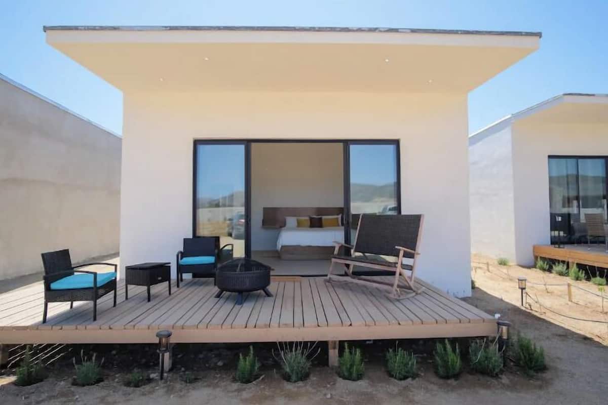 Um terraço moderno ao ar livre com área de estar e lareira, que dá acesso a um quarto com uma grande porta de correr.