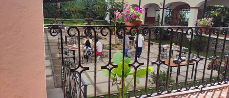 Un área de patio al aire libre con mesas y sillas, rodeada de macetas con plantas y una fuente.