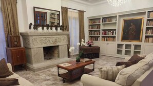Uma sala de estar com lareira, um conjunto de sofás, uma mesa de centro e uma estante de livros.