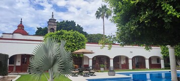Un patio con piscina, zona de comedor y edificio con cúpula roja y torre del reloj.