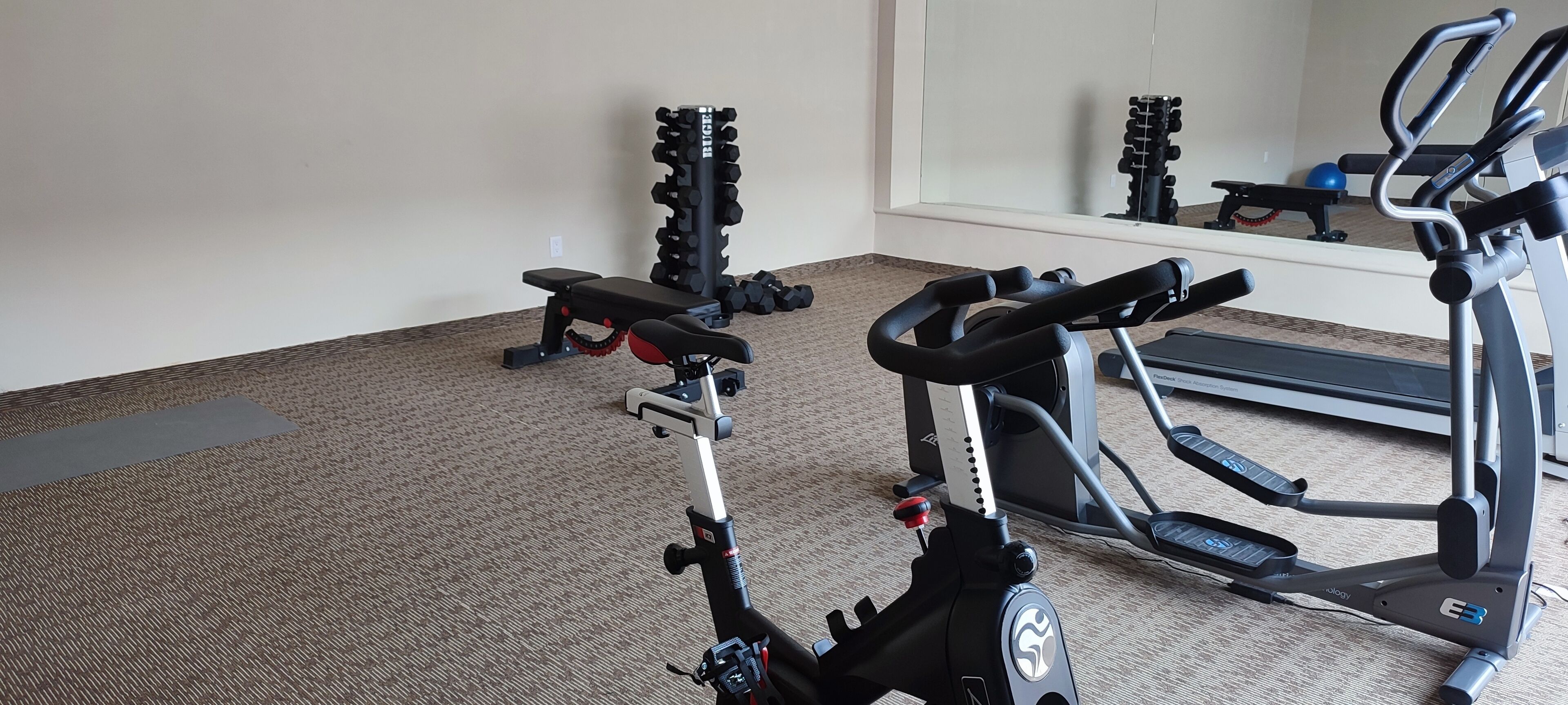 Un gimnasio con equipo de ejercicio, incluyendo una cinta de correr, una máquina elíptica y un banco de pesas.