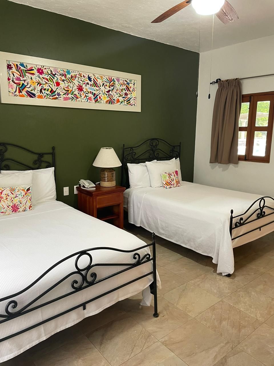 Habitación de hotel con dos camas, ventilador de techo, teléfono en la pared y ventana con cortinas.