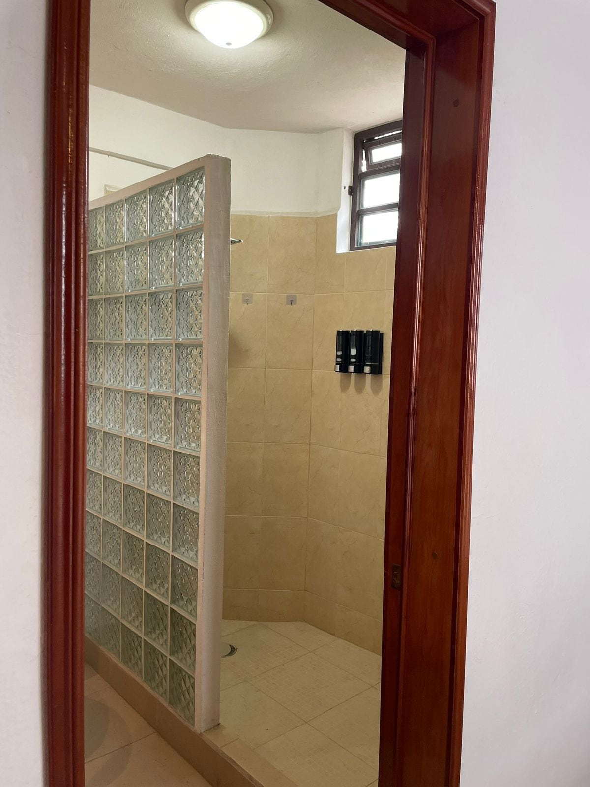 Un baño con cabina de ducha de vidrio, baldosas color beige y una ventana.