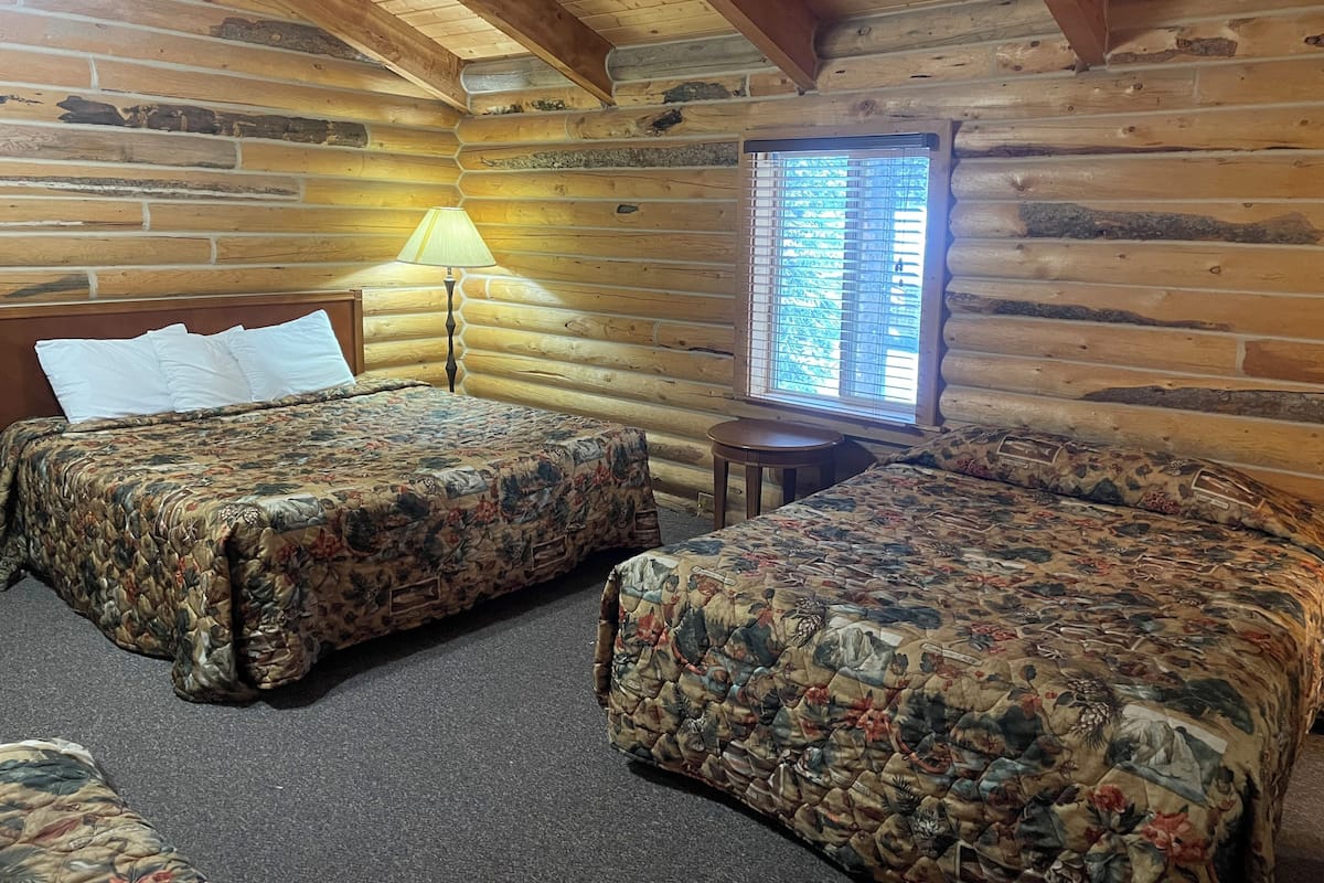 A log cabin room with two beds, a lamp, and a window.