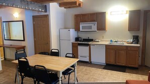 A compact kitchen with wooden cabinets, a white refrigerator, a microwave, a stove, and a dishwasher. There is a dining table with chairs and a small rug on the floor. - Bear Lodge Resort (Dayton)