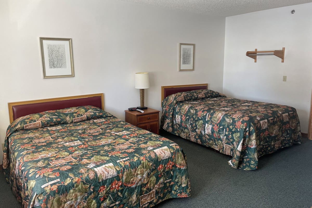 A hotel room with two beds, each with floral-patterned bedding, a bedside table with a lamp, and framed artwork on the walls.