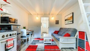Una cucina compatta con fornello, microonde e forno. È presente una zona pranzo con tavolo e sedie. In zona living si vedono un divano e una scala.