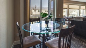 A glass-top dining table with four chairs, a potted plant, and a view of buildings through a sliding glass door. - Rockaway Beach Vacation Rental Near Beach Access! (Rockaway Beach)