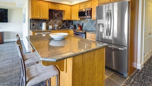 A modern kitchen with wooden cabinets, granite countertops, stainless steel appliances, and a large island with bar stools. - Rockaway Beach Vacation Rental Near Beach Access! (Rockaway Beach)