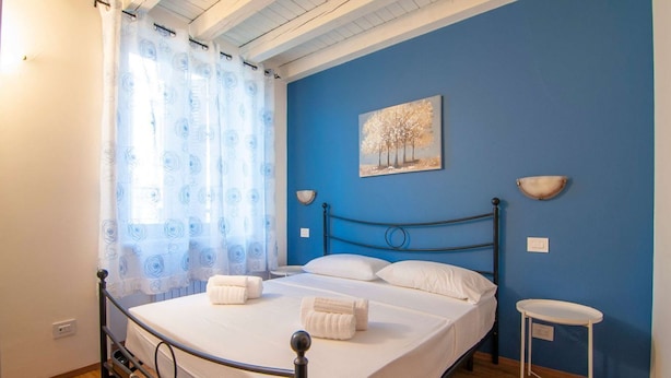 Ein Schlafzimmer mit Bett, Nachttisch, einem Gemälde und einem Fenster mit Vorhängen.