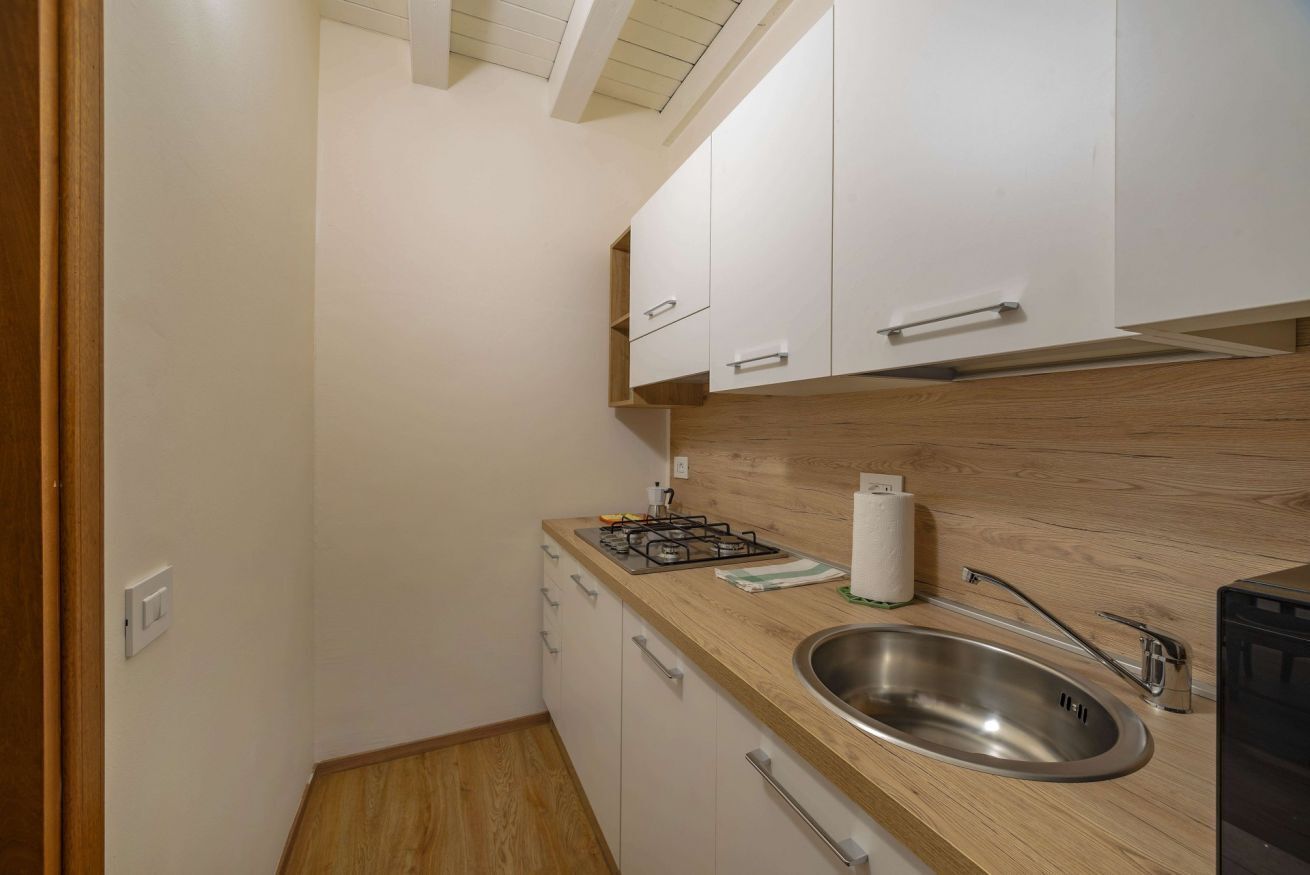 Une cuisine compacte avec des meubles blancs, un plan de travail en bois, un évier en acier inoxydable et une cuisinière à gaz.