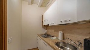 Eine kleine Küche mit weißen Schränken, einer Holz Arbeitsplatte, einer Edelstahl-Spüle und einem Gasherd.