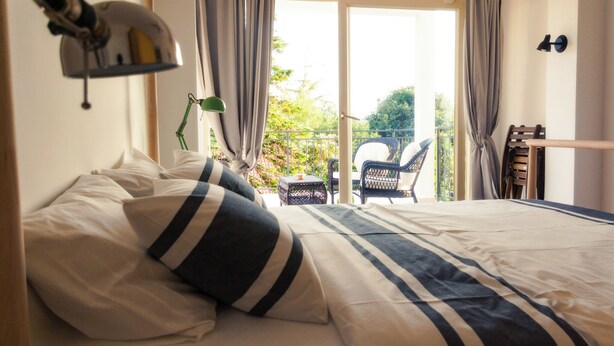 Un lit bien fait, avec une literie à rayures, une petite table avec une lampe et une chaise placée devant un balcon orné de rideaux.