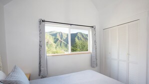 Ett sovrum med en stor säng, ett fönster med utsikt över bergen och en vit garderob.