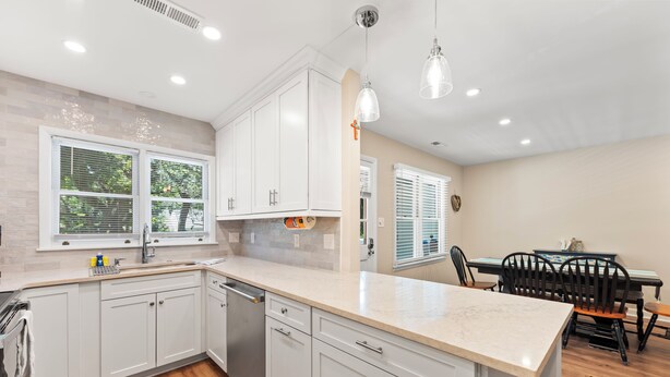 A modern kitchen with white cabinets, a marble countertop, and a dining area with a table and chairs.