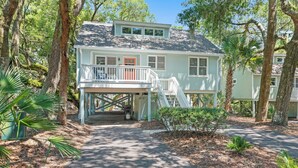 A two-story house with a covered porch and a small deck, surrounded by trees and vegetation.