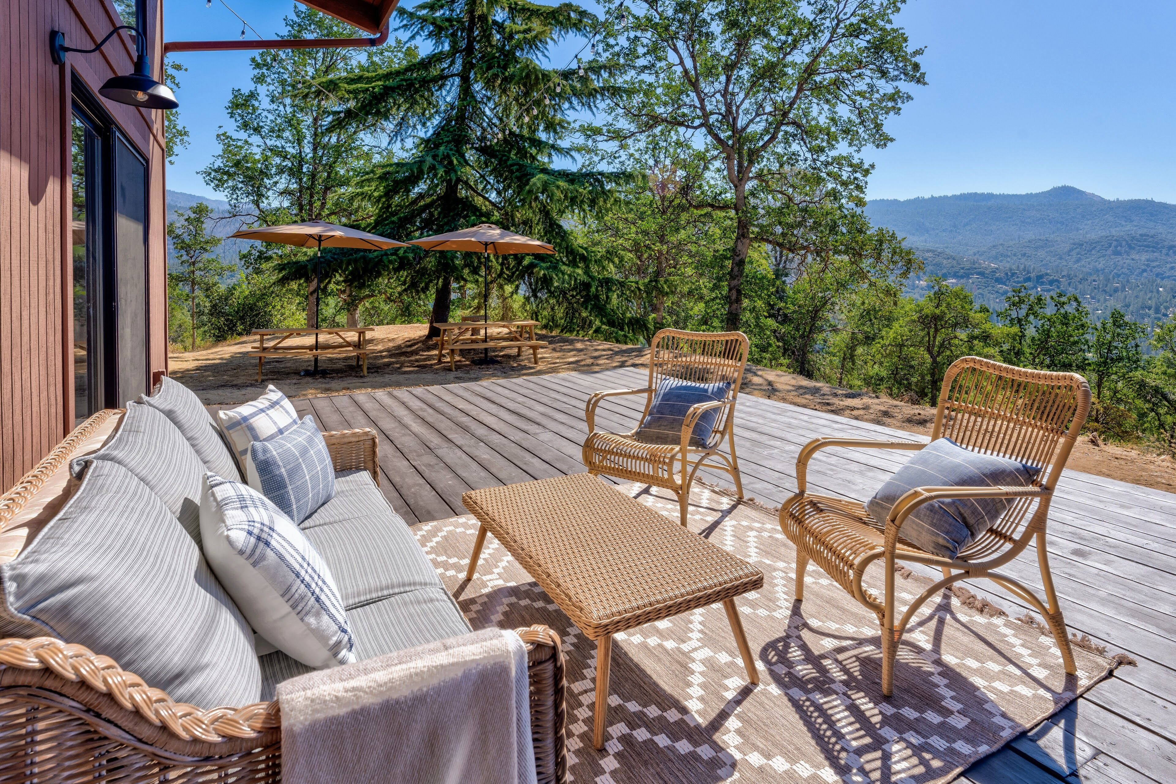 A wooden deck with wicker furniture, including a sofa and chairs, overlooking a mountainous landscape.