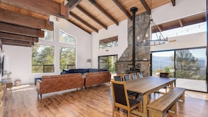 A spacious living area with a wooden dining table, benches, and a stone fireplace. - Yosemite Sunrise House with hot tub/views/game room! (Oakhurst)