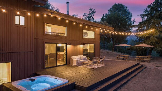A wooden deck with a hot tub, outdoor furniture, and string lights. - Yosemite Sunrise House with hot tub/views/game room! (Oakhurst)