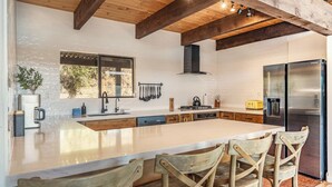 A modern kitchen with a large island, wooden chairs, and a stainless steel refrigerator. - Yosemite Sunrise House with hot tub/views/game room! (Oakhurst)