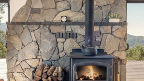 A stone fireplace with a black chimney, logs, and a clock on the wall. - Yosemite Sunrise House with hot tub/views/game room! (Oakhurst)