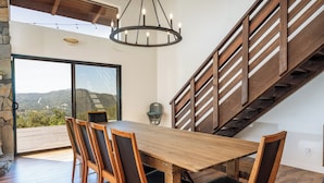 A dining area with a wooden table and chairs, a chandelier, a staircase, and a view of the outdoors. - Yosemite Sunrise House with hot tub/views/game room! (Oakhurst)