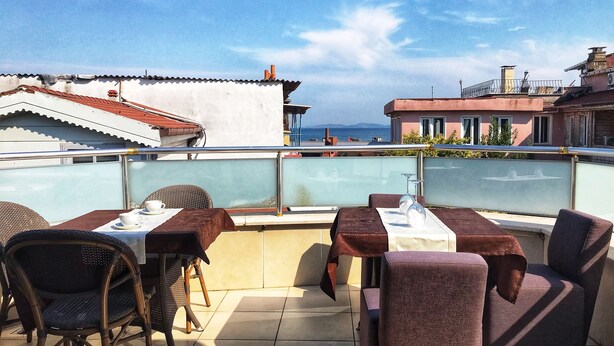A rooftop terrace with outdoor seating, a view of the sea, and surrounding buildings. - Yed Hotel (Istanbul)