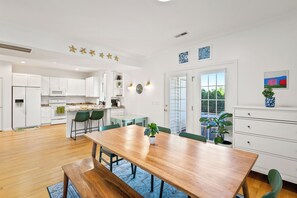 Une cuisine moderne avec des meubles blancs, une table à manger en bois et une grande fenêtre.
