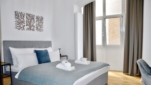 A modern hotel room with a large bed, a nightstand, a chair, and a window with curtains. - Spacious Design Retreat for Groups & Families (Stuttgart)