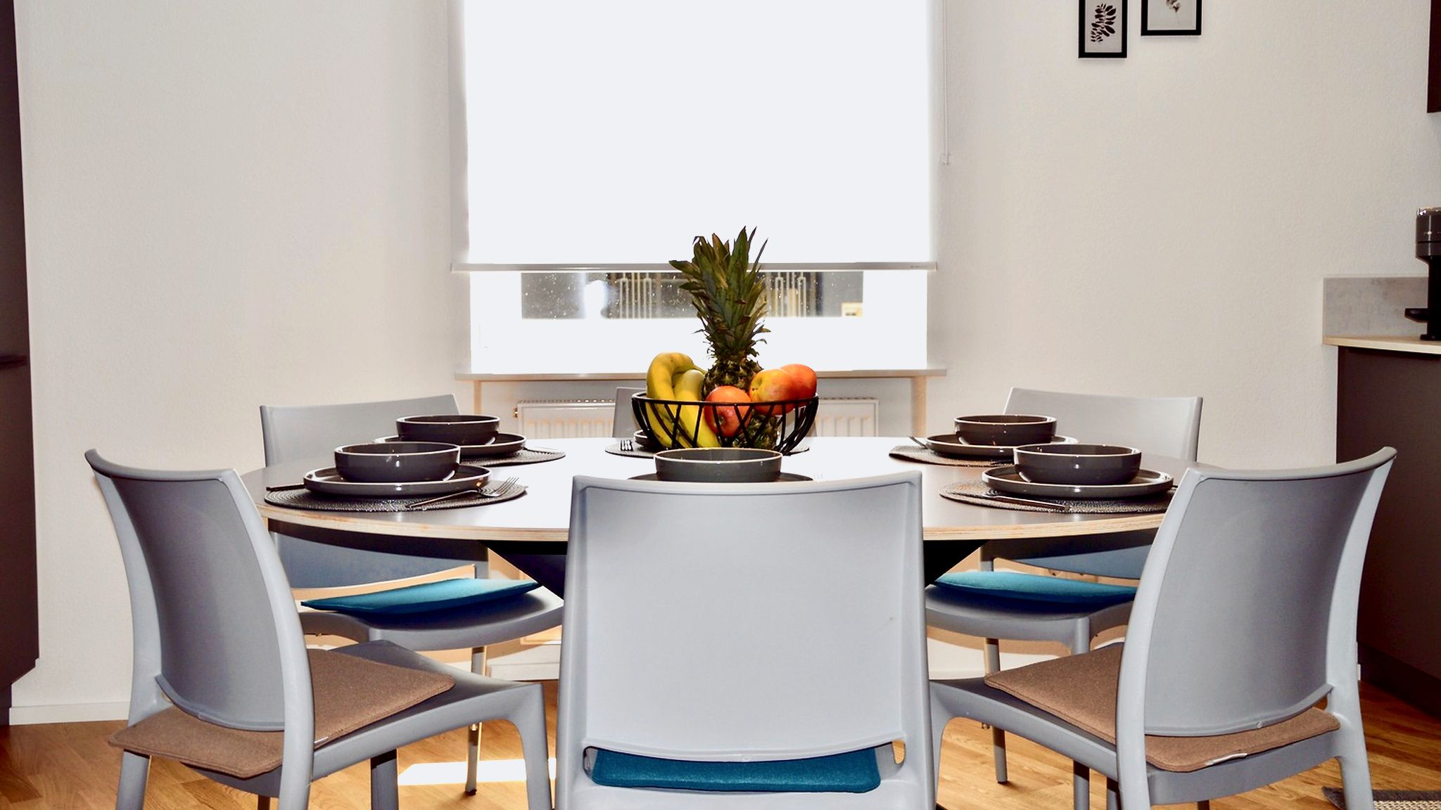 A modern dining area with a round table, six chairs, and a fruit bowl.